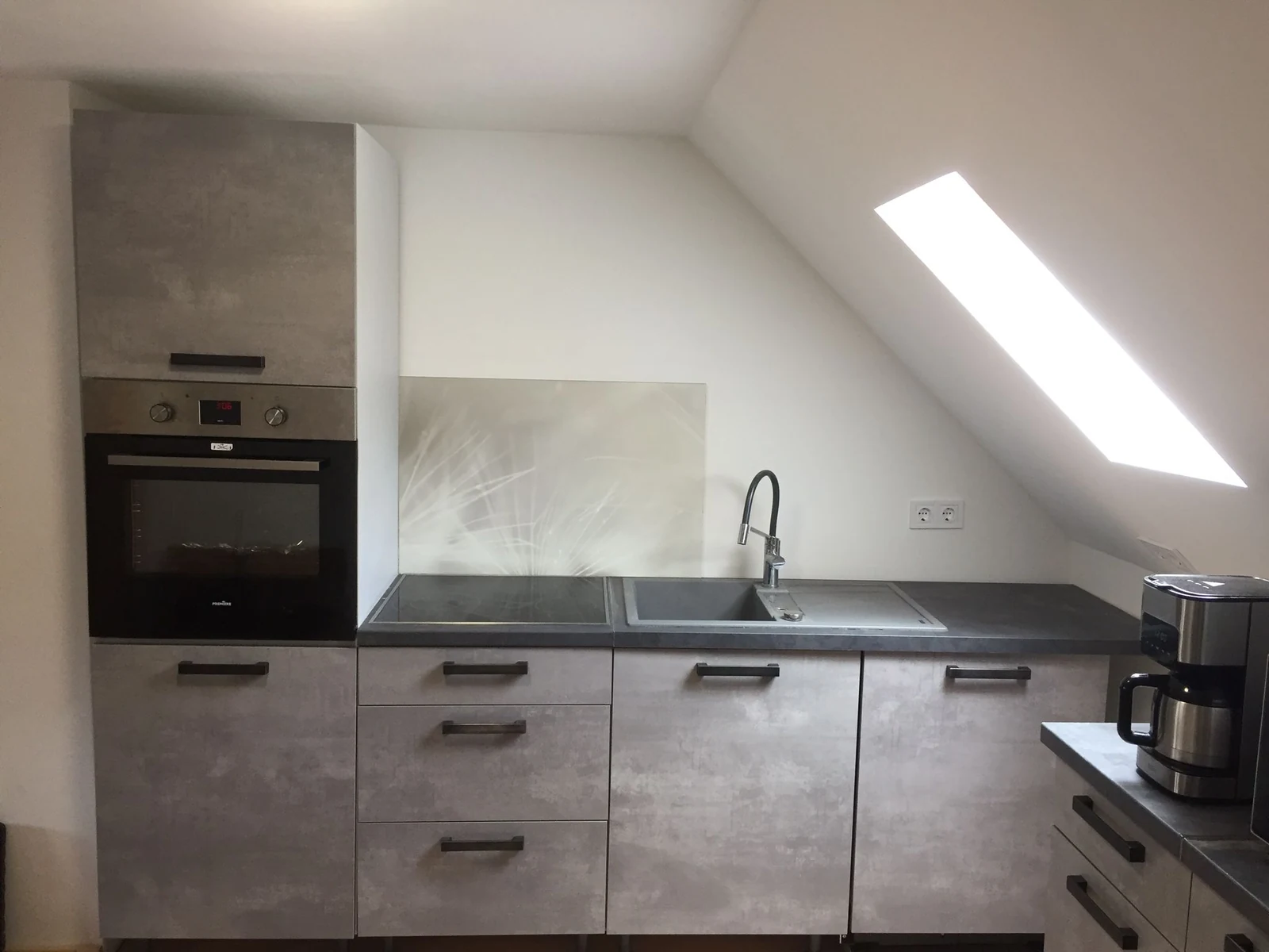 Montierte graue Küchenzeile unter der Dachschräge mit Backofen, Kochfeld und Spüle