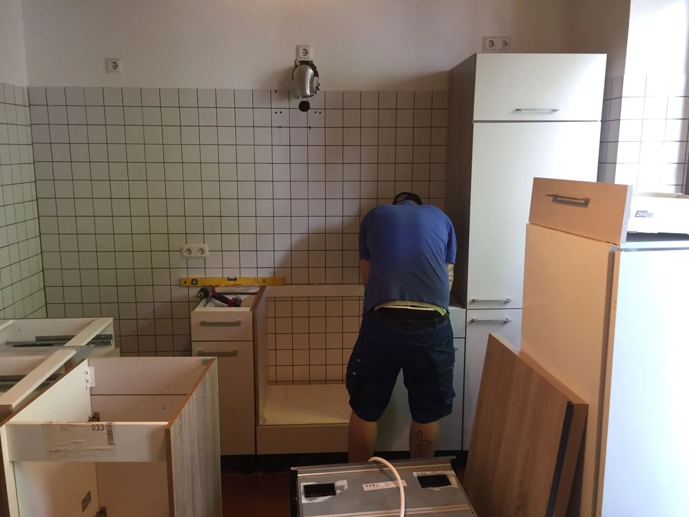 Monteur bei der Arbeit an Küchenunterschränken, daneben Wasserwaage und Werkzeug