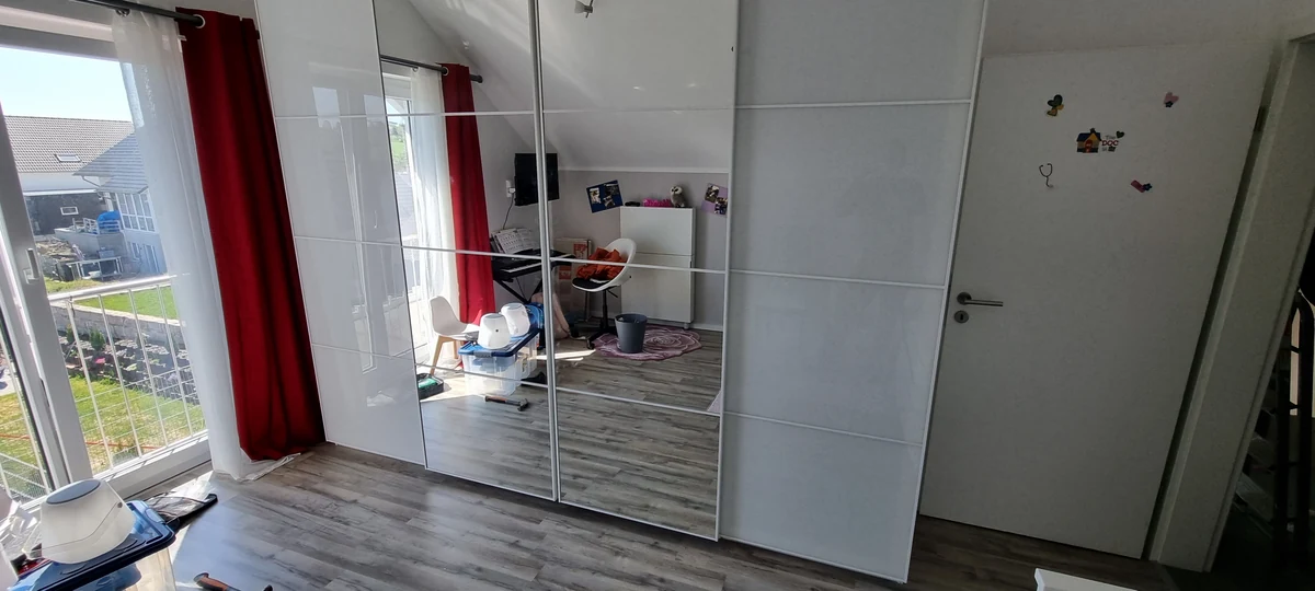 Aufgebauter weißer Kleiderschrank mit eingesetzten Spiegel- und Schiebetüren