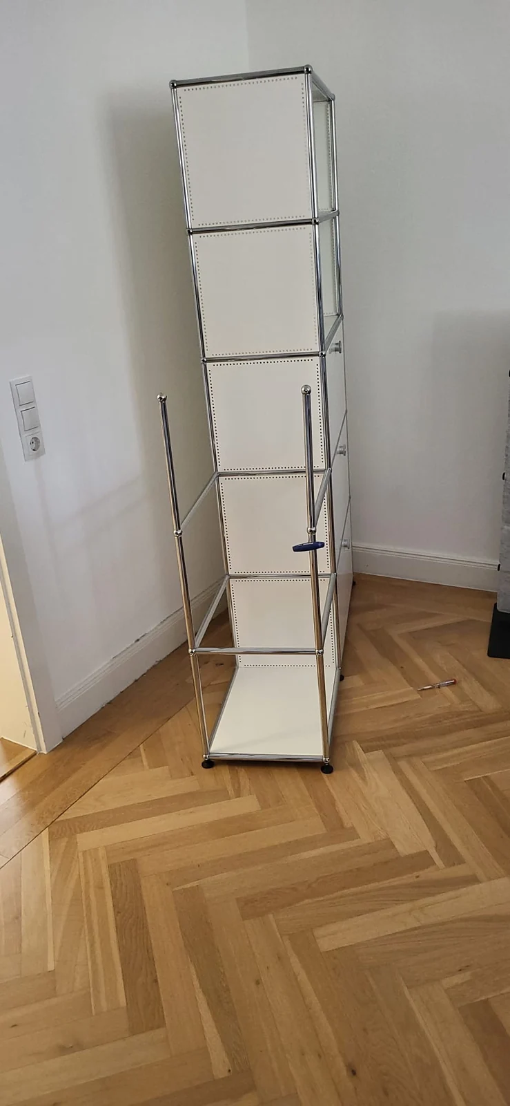 Hohes weißes USM-Haller-Regal mit teilweise offenem Metallgestell während der Montage