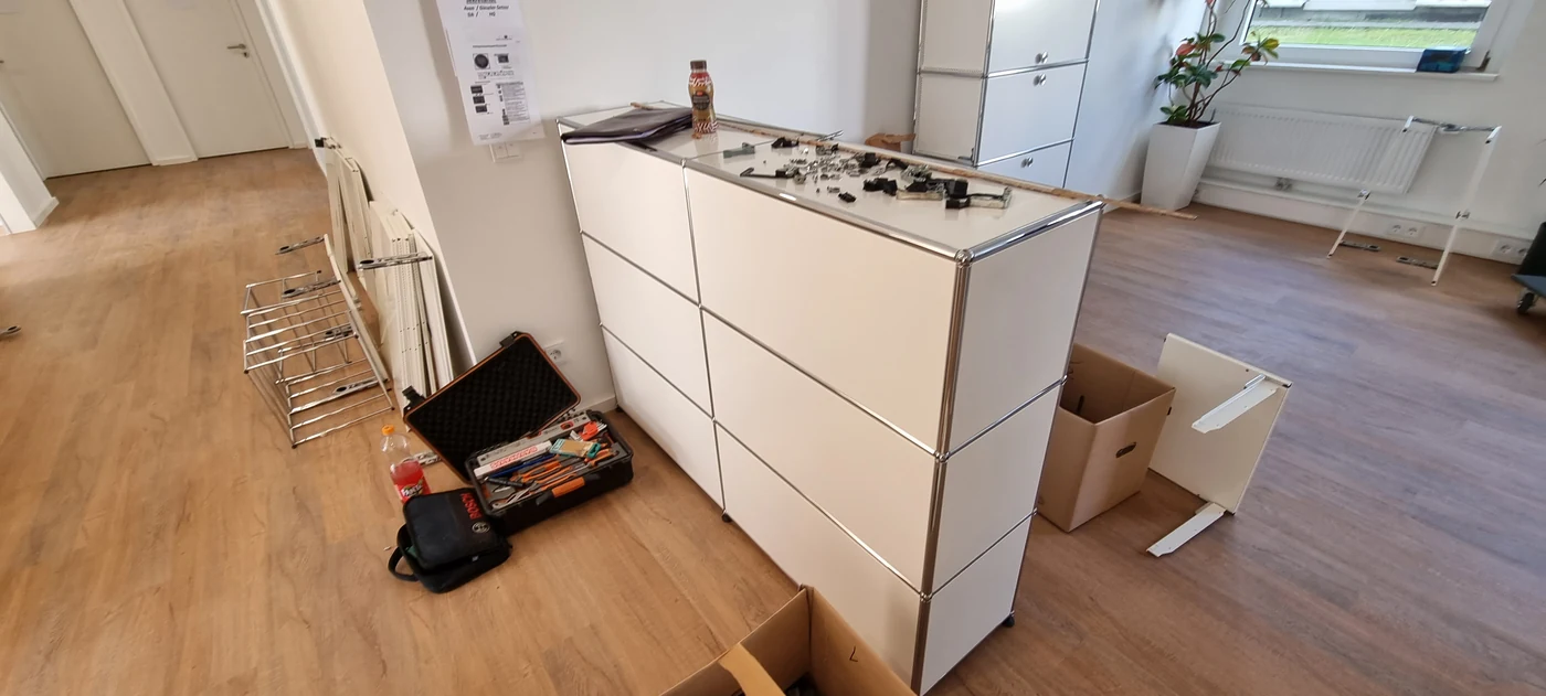 Weiße USM-Haller-Möbel mit bereitgelegten Bauteilen und geöffnetem Werkzeugkoffer